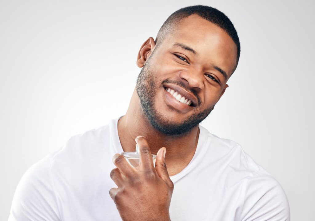 Studio portrait of a handsome young man spraying perfume on himself against a white background
